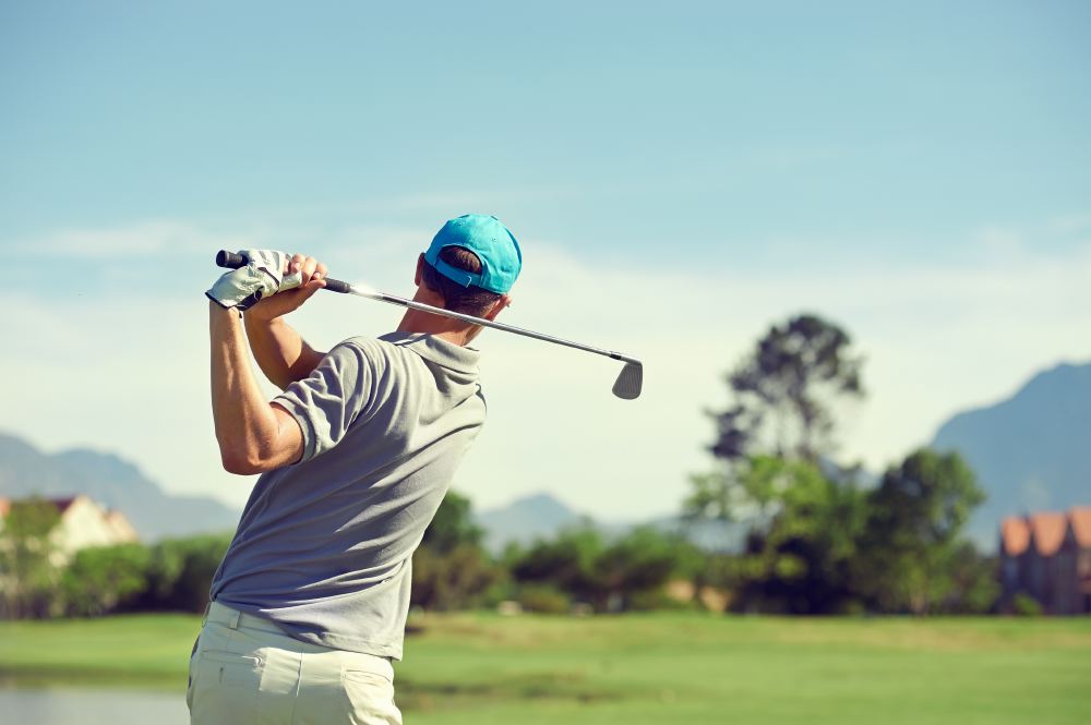 A golfer in a blue cap swings a club on a sunny golf course, showcasing a high-quality sports travel experience.
