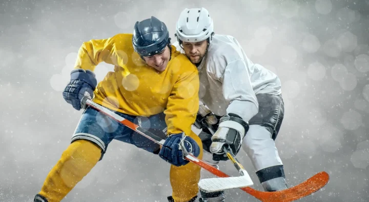 Two hockey players in yellow and white jerseys compete intensely for the puck under snowy conditions, ideal for those considering hockey travel and ticket packages for major events.