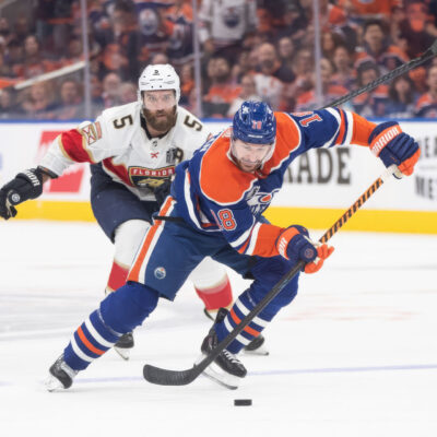 Two hockey players from the Panthers and Oilers compete for the puck in an intense moment of a game, highlighting their speed and focus, perfect for fans looking into Stanley Cup Final travel packages.