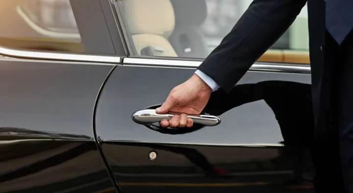 A person in a suit opens a black car door, symbolizing premium luxury travel services with Roadtrips, the ultimate in sports travel.
