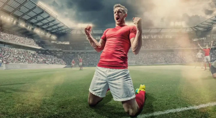 Excited soccer player celebrating on the field in a stadium, representing the thrilling sports travel experiences offered by Roadtrips.
