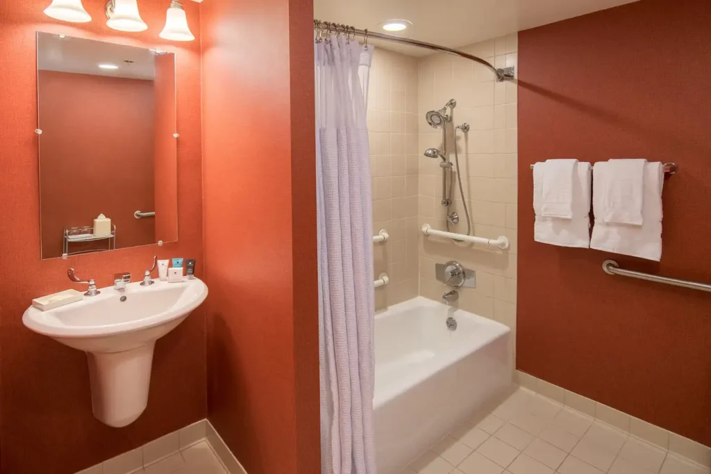 Bright bathroom featuring a sink, mirror, bathtub with a shower, and towel rack in the Cabana Hotel Palo Alto, a location popular for Super Bowl accommodations in the Palo Alto and San Jose area.