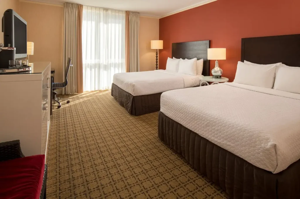 Book a stay at the Cabana Hotel in Palo Alto, showcasing a spacious room with two double beds, tastefully decorated with a red and cream color scheme, ideal for visitors looking for luxury hotels near San Jose.