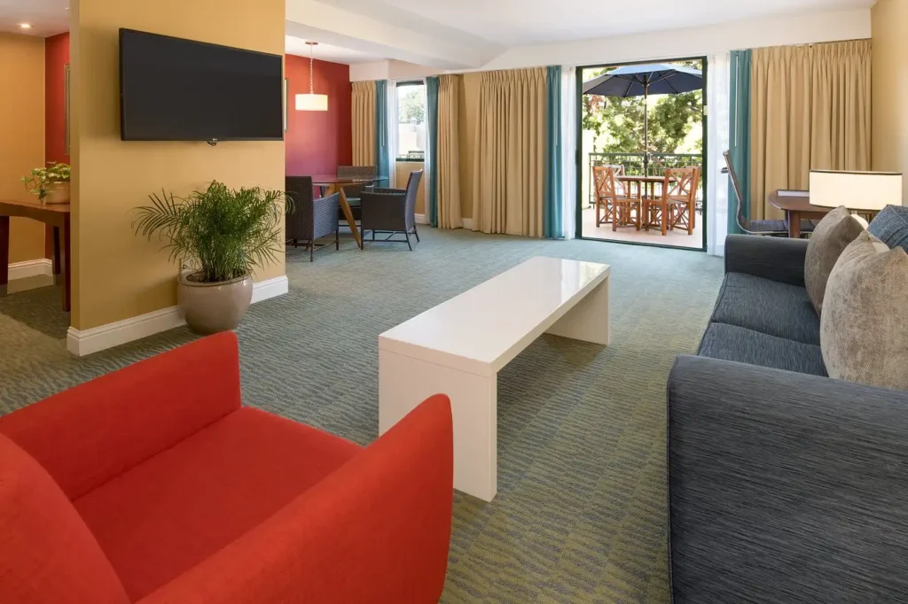 Spacious suite at Cabana Hotel in Palo Alto featuring a cozy seating area, modern dining space, and a balcony overlooking lush greenery, ideal for South Bay Area accommodations.