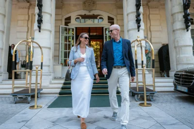 A mature couple happily exits a luxury hotel, engaging in conversation, representing a high-end sports travel package experience.