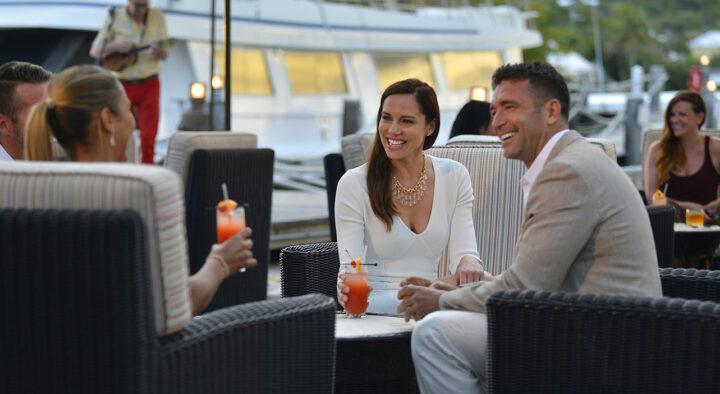 Groups of people enjoy drinks and converse in an outdoor lounge by the marina, capturing the inviting atmosphere often highlighted in testimonials for leisure and travel experiences like roadtrips.