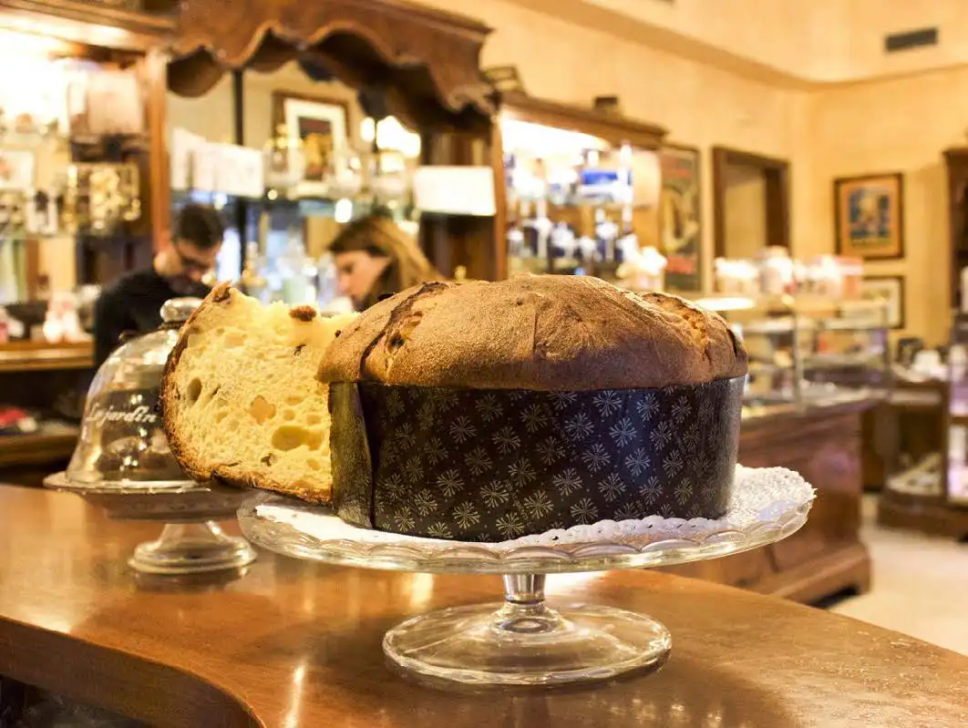 A traditional Italian panettone displayed on a glass stand in a bustling Milanese café, capturing a slice of the local Milan Food Adventure.