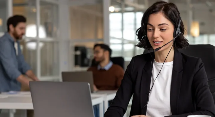 Woman wearing a headset provides expert pre-travel assistance at a service desk, surrounded by colleagues, enhancing high-quality sports travel experiences.