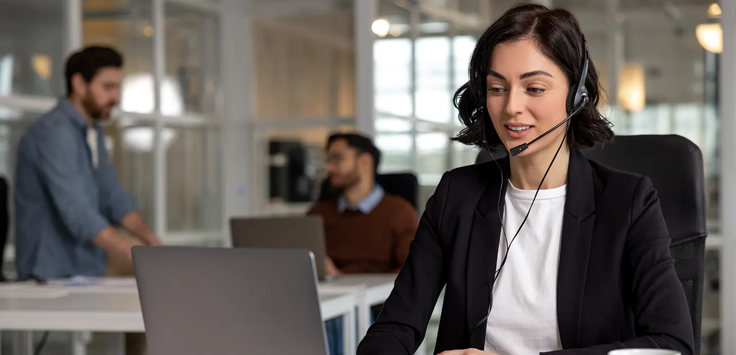 Woman wearing a headset provides expert pre-travel assistance at a service desk, surrounded by colleagues, enhancing high-quality sports travel experiences.