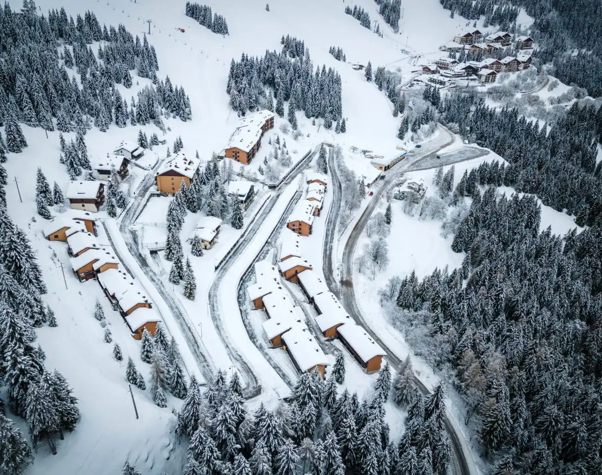 Snow-covered chalets and winding roads in a mountainous area near Milan, ideal for a winter skiing adventure and exploring Milan highlights.