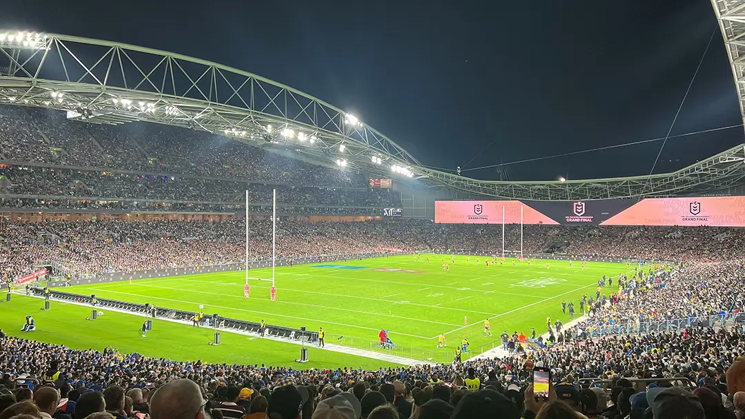 A vibrant night-time rugby match with a packed stadium under bright lights, showcasing a key venue for the World Cup of Rugby Host Cities and Venues event.