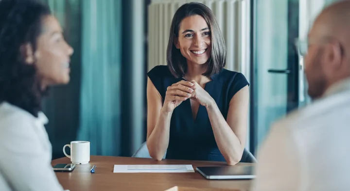 A smiling woman in a business meeting with two colleagues, discussing topics possibly related to travel advice or event planning for White Label Brochures.