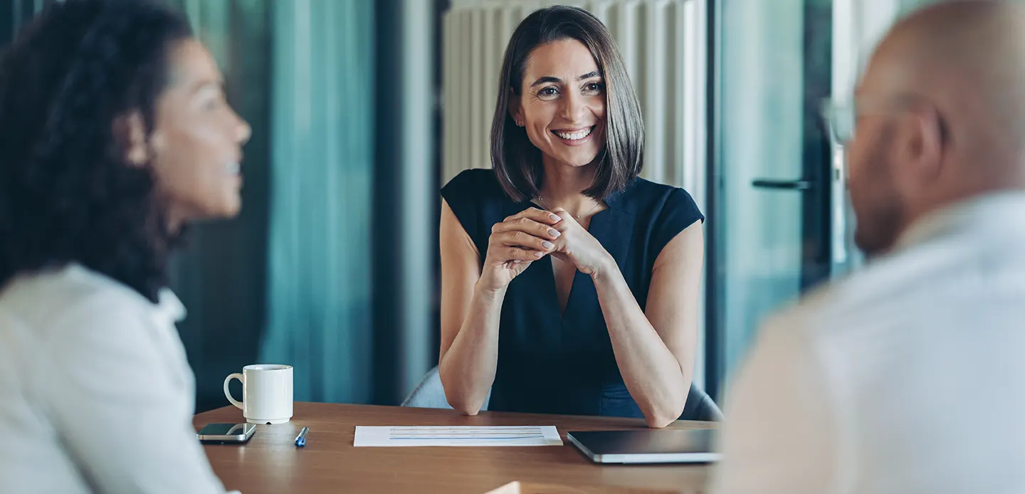 A smiling woman in a business meeting with two colleagues, discussing topics possibly related to travel advice or event planning for White Label Brochures.