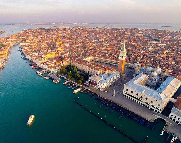 Aerial view of Venice featuring the iconic St. Mark's Square and Basilica, with boats navigating the adjacent Grand Canal.